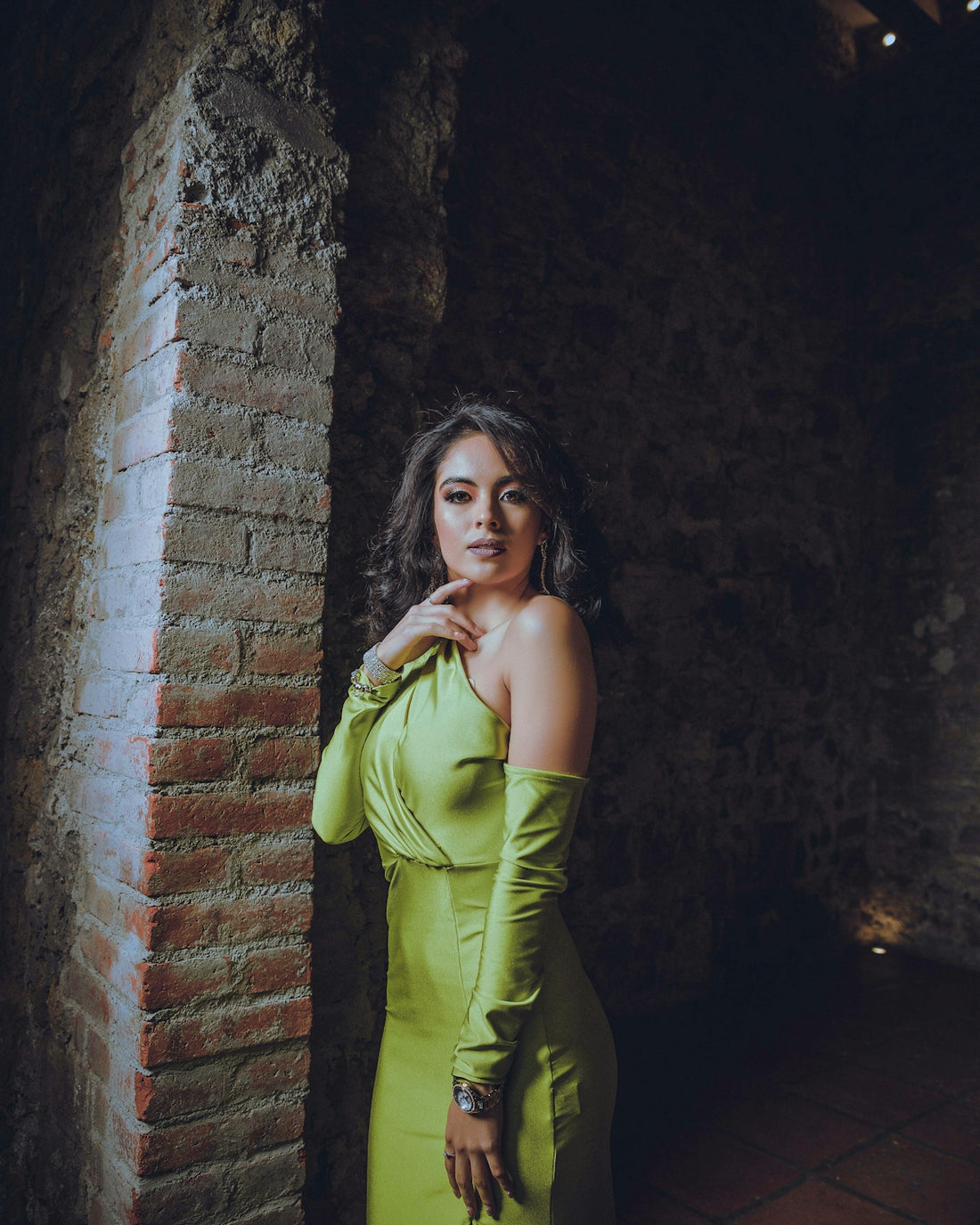 woman in green sleeveless dress leaning on brown brick wall