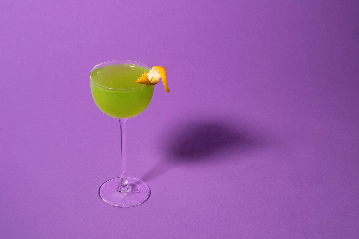 a green drink with a slice of orange on the rim