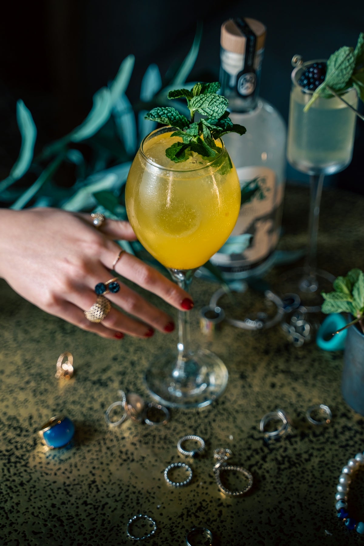 a woman's hand holding a cocktail glass with a green garnish on