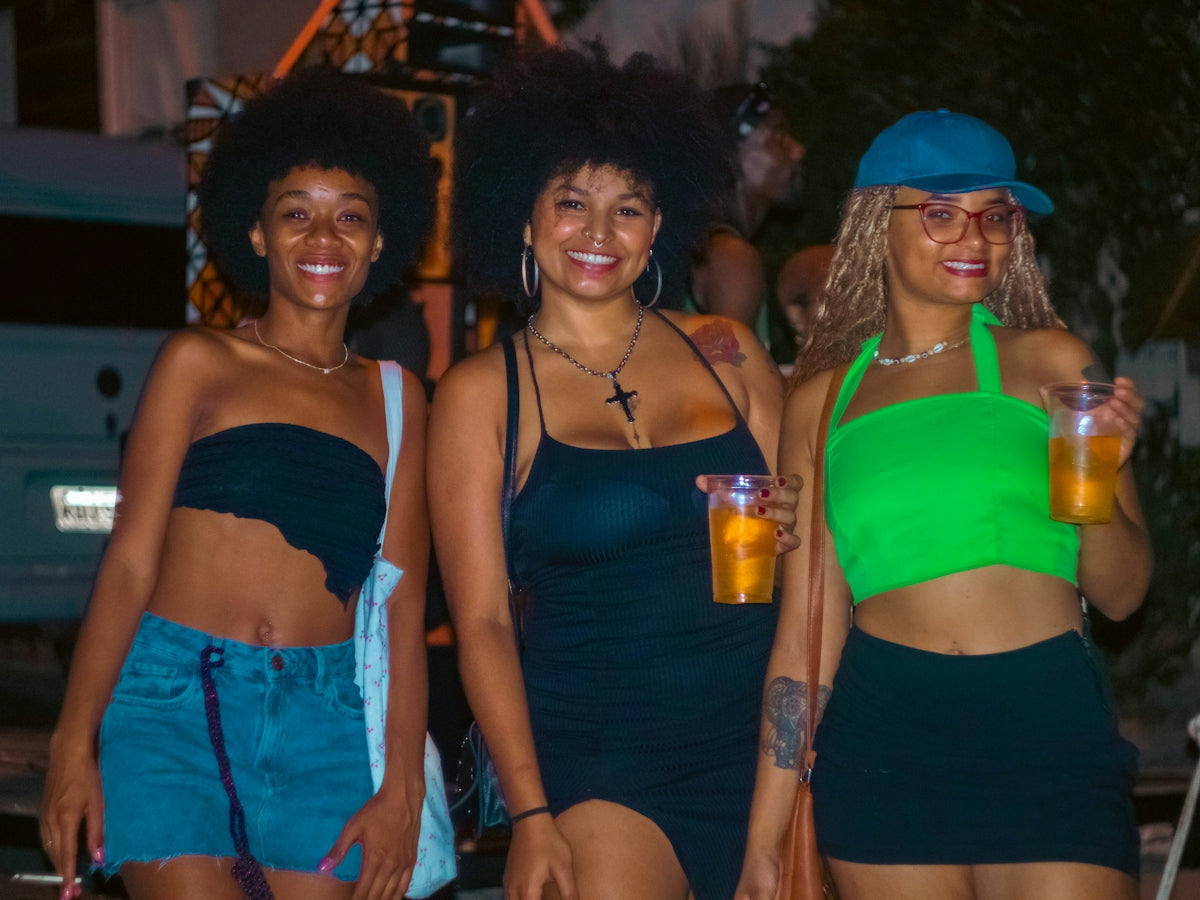 Three friends are smiling and holding drinks together