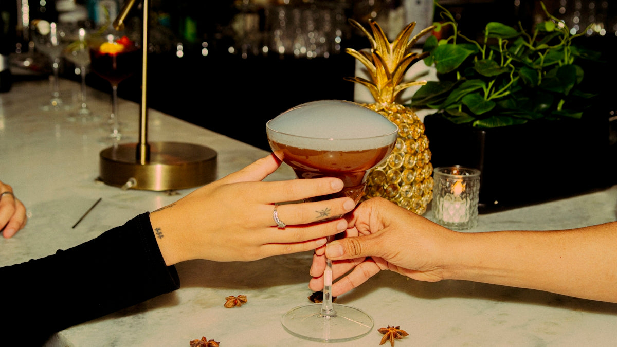 A cocktail is being passed between two hands.