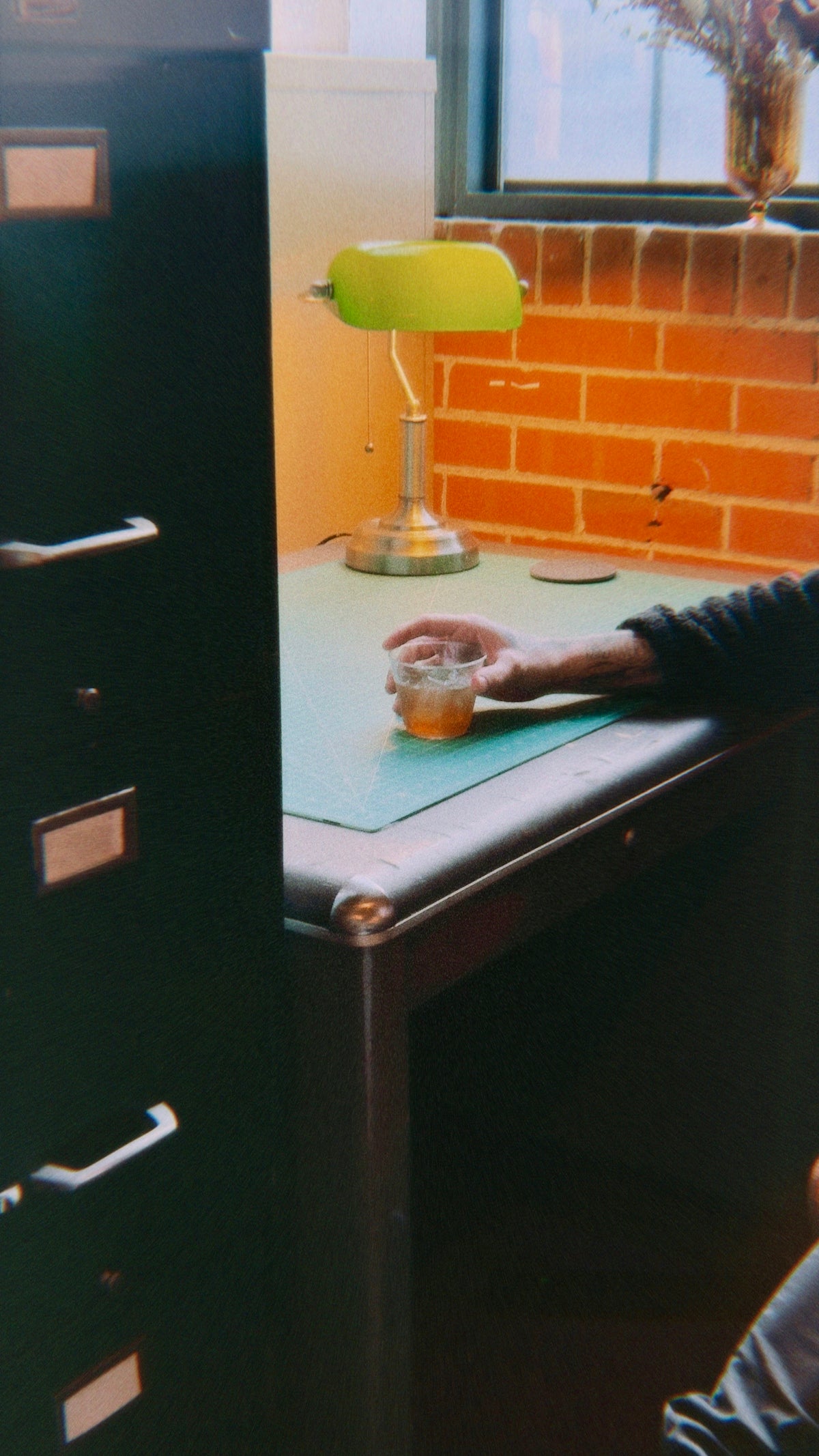 Person holds a drink at their desk with a lamp.