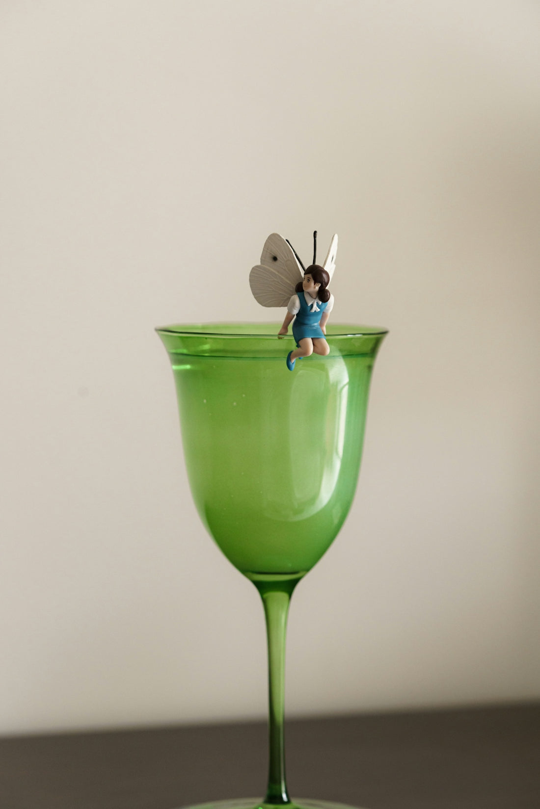 A fairy sits atop a green wine glass.