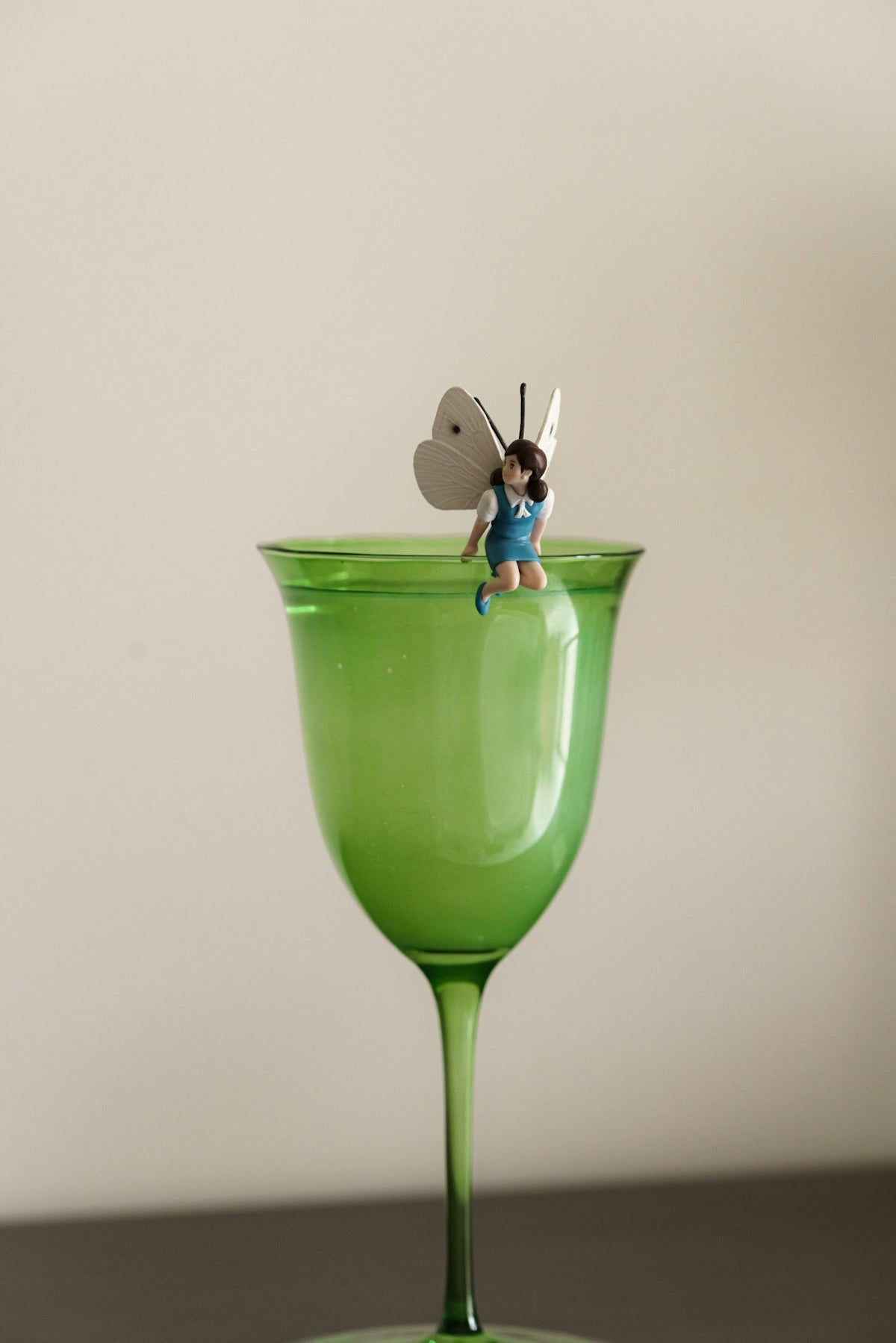 A fairy sits atop a green wine glass.