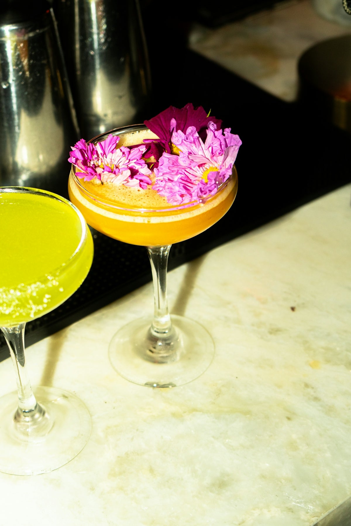 Cocktails are garnished with flowers on a marble surface.