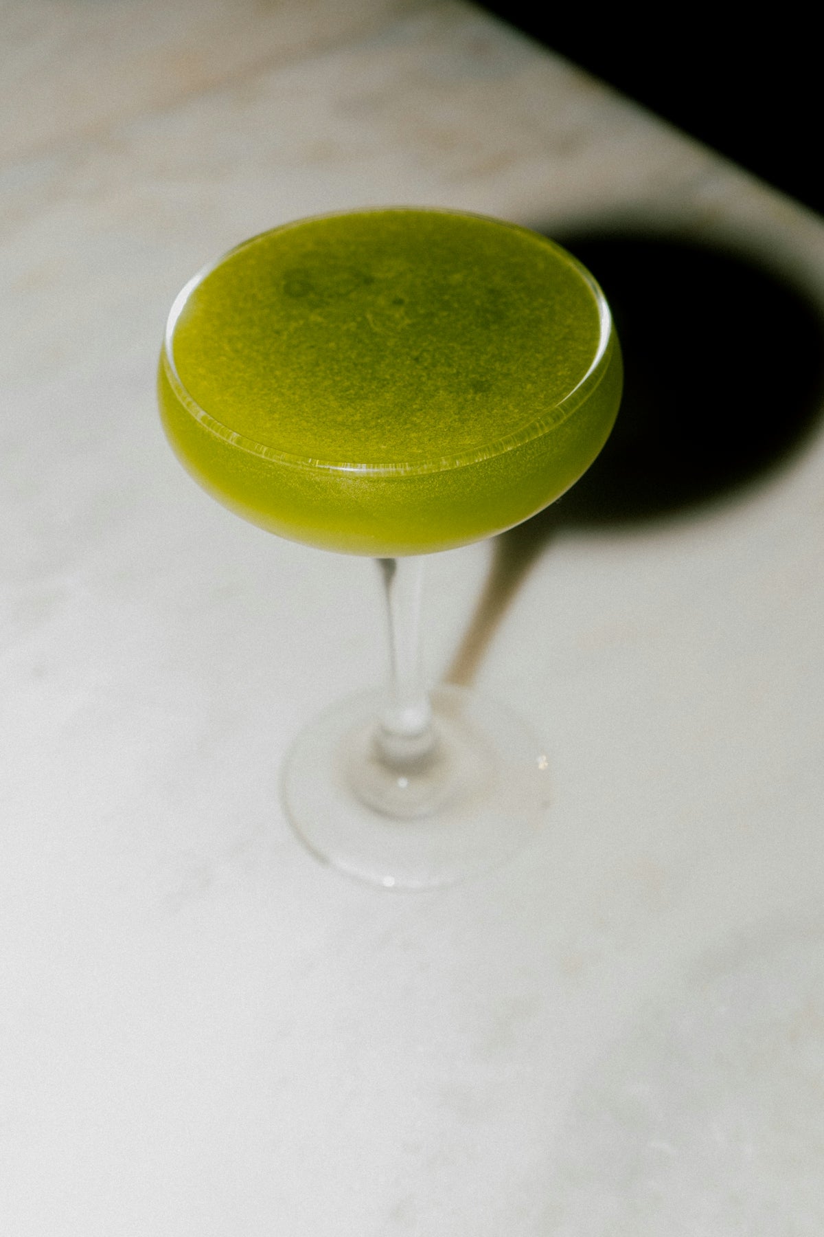 A green cocktail sits in an elegant glass.