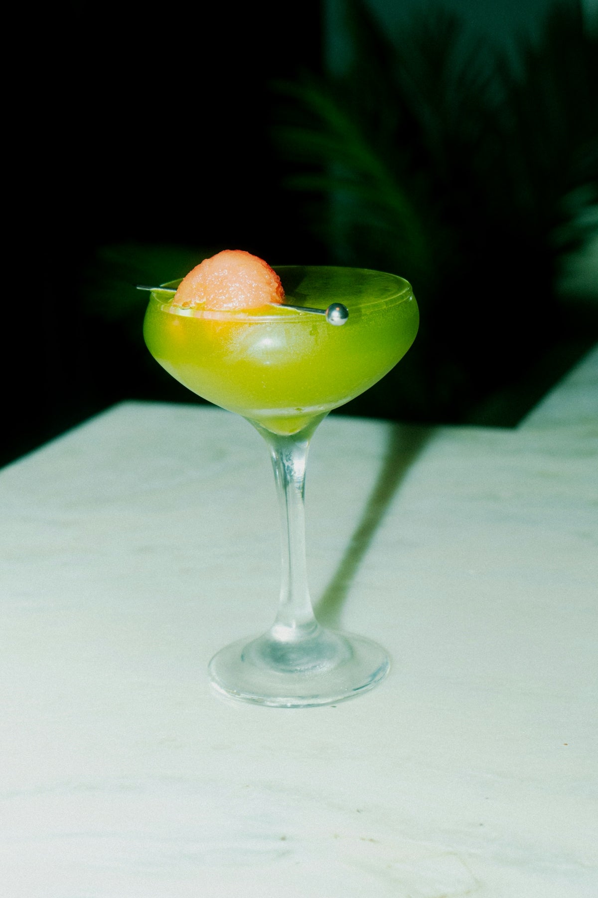 A green cocktail garnished with melon.