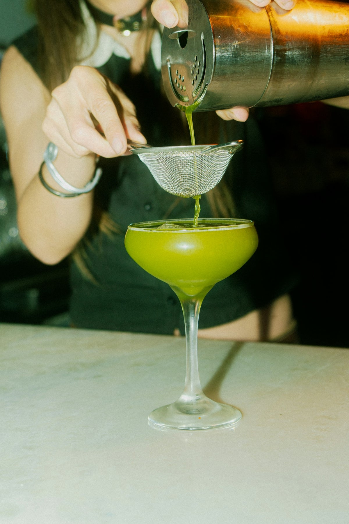 A bartender strains a vibrant green cocktail.