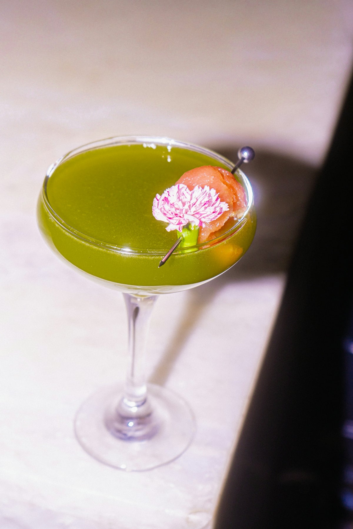 A green cocktail garnished with a flower.