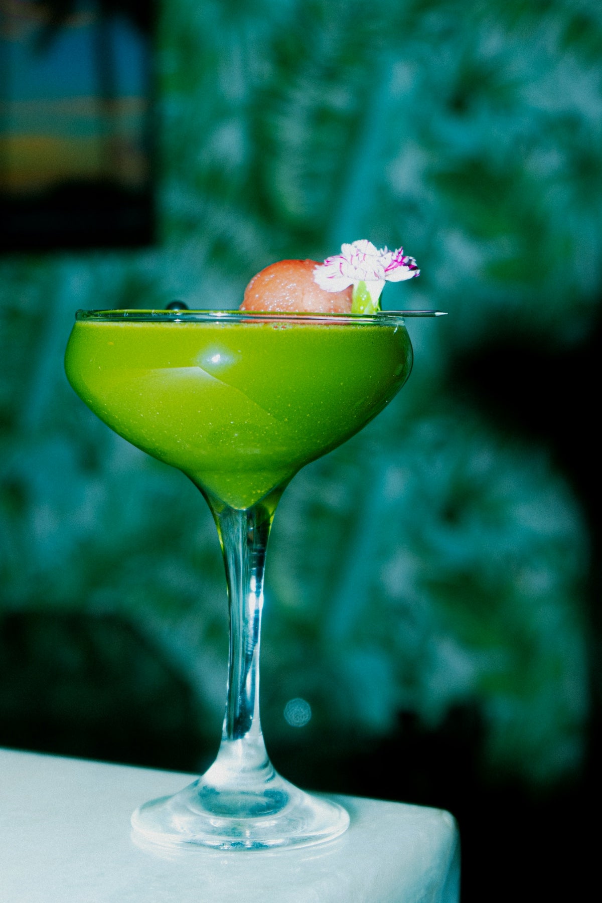 A green cocktail is garnished with flowers and fruit.