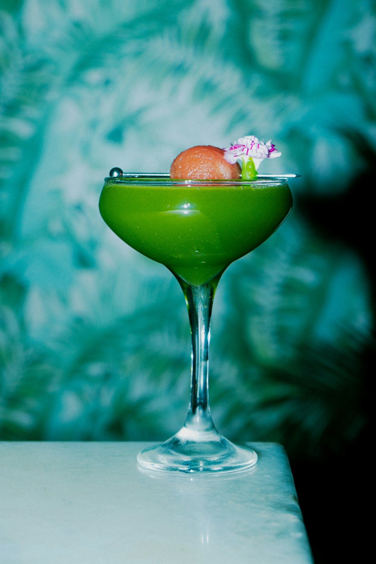 A green cocktail is garnished with fruit and flowers.