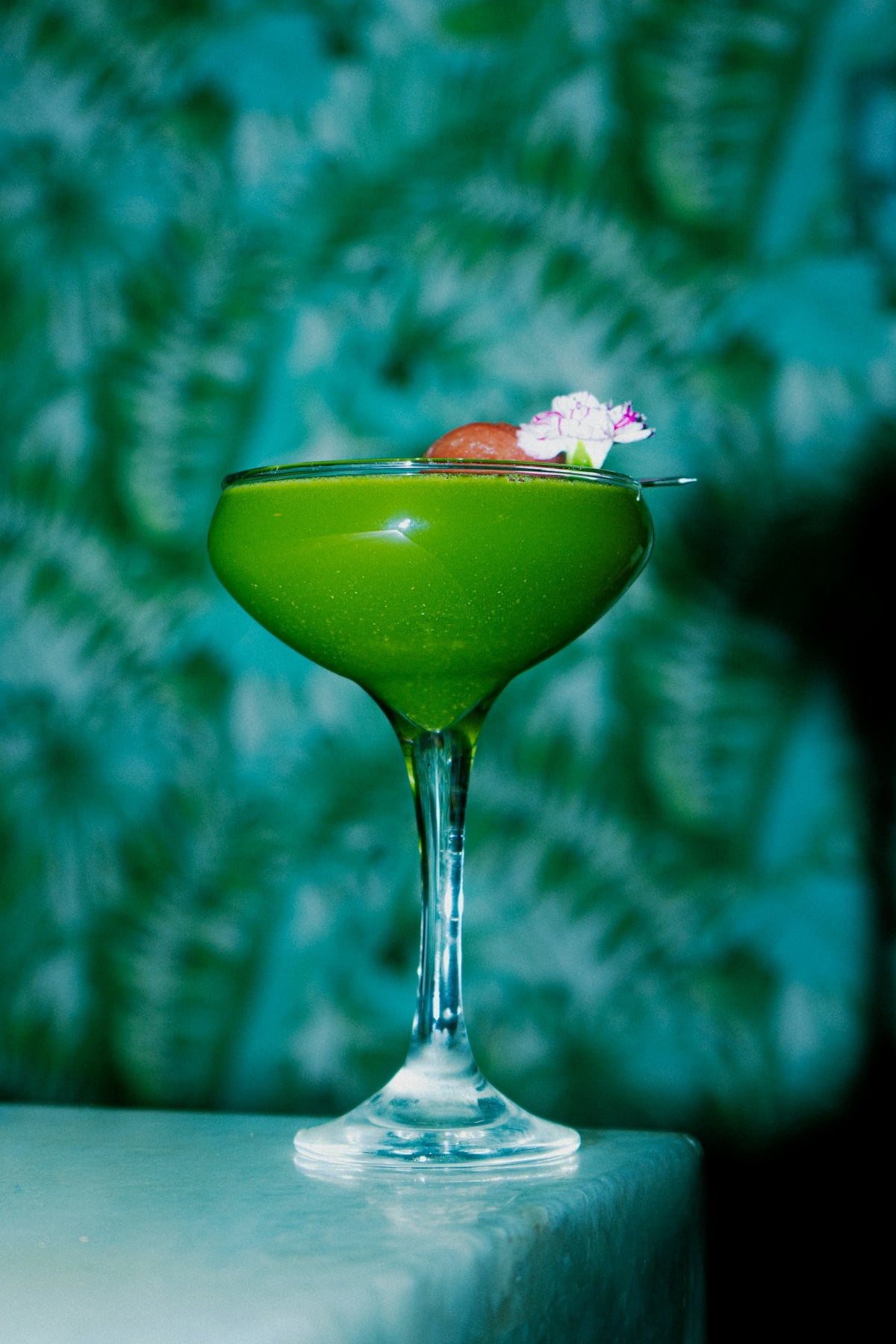 A green cocktail is garnished with a flower.