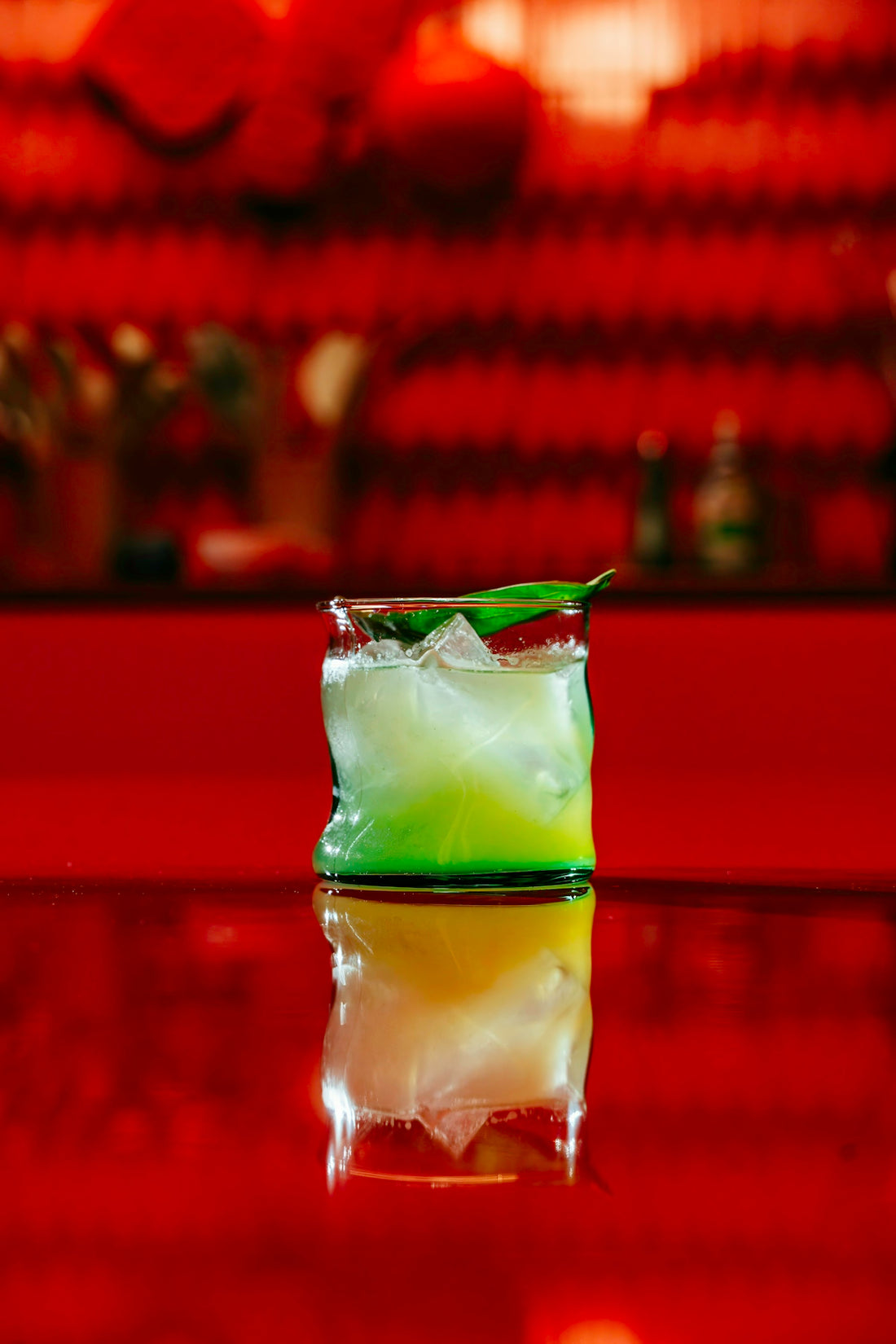 A green cocktail reflects on a red surface.