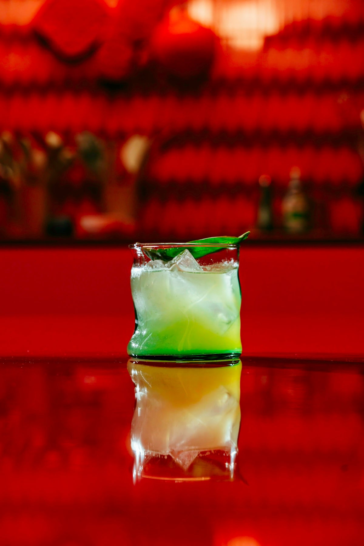 A green cocktail reflects on a red surface.