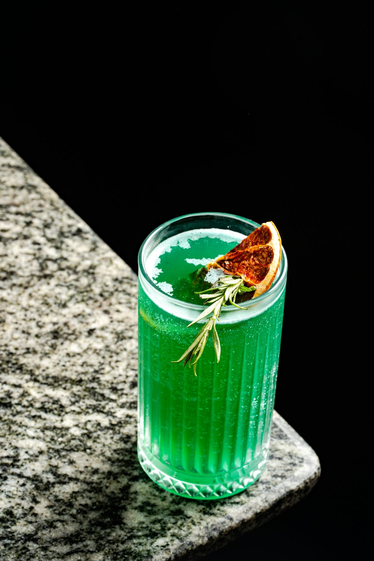Green cocktail with orange slice and rosemary garnish