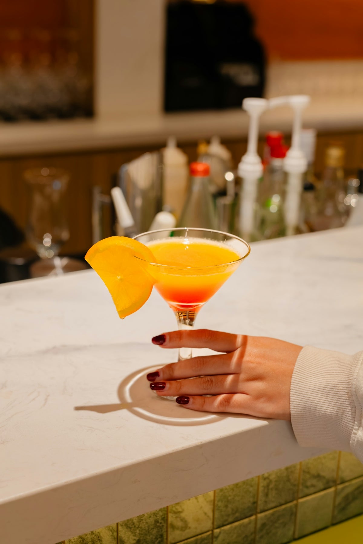 A colorful cocktail with an orange slice garnish.