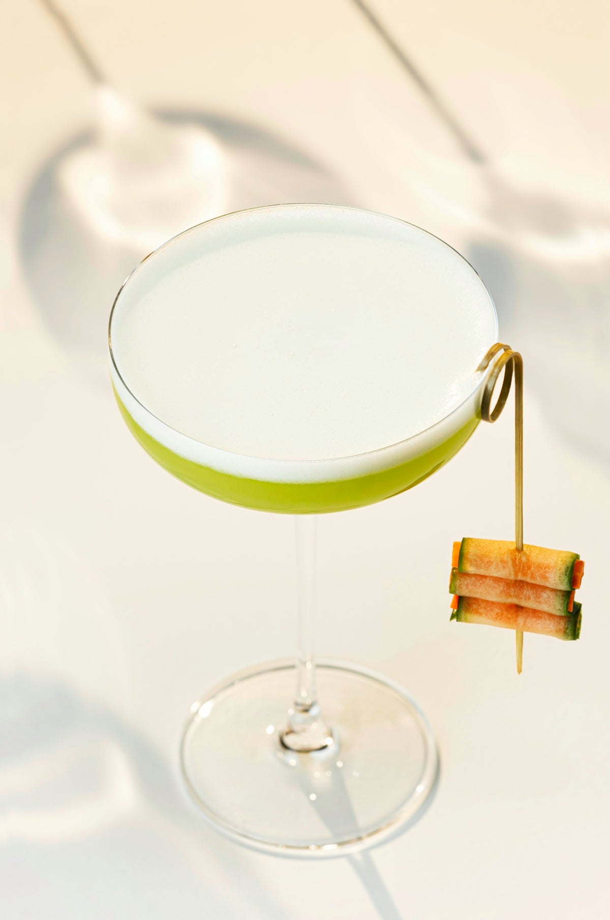 A green cocktail with a fruit garnish