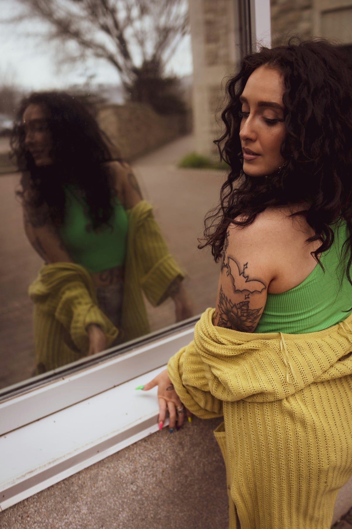 Woman with dark curly hair and tattoos by window