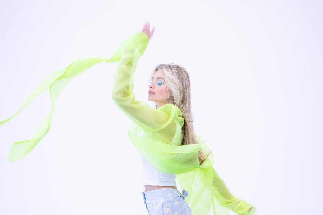 Blonde woman in white top with flowing green fabric.