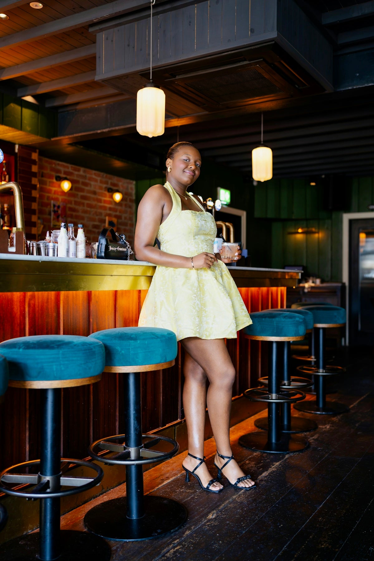 A woman in a yellow dress holding a cocktail at a bar counter